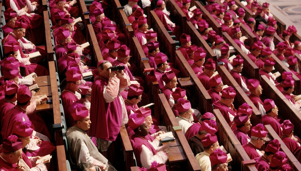 II. Vatikanisches KonzilBild: Die Bischöfe (Konzilsväter) auf ihren Plätzen in der Konzilsaula in der Peterskirche. Ein Bischof schaut durch ein Fernglas.